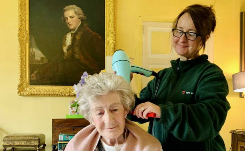 carer pushing an elderly ladyn throiygh a blossom feild in a wheelchair