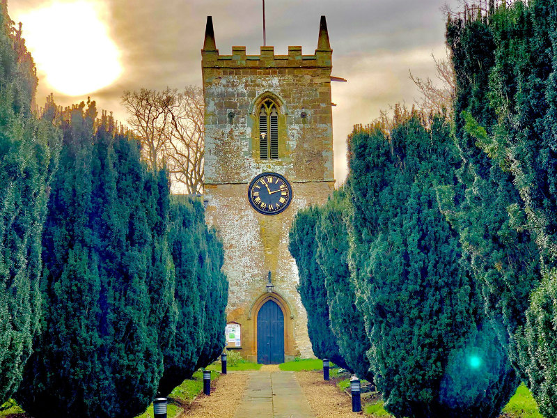 Historic church tower with clock between tall cypress trees