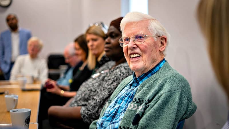 Elderly man smiling in community meeting discussion