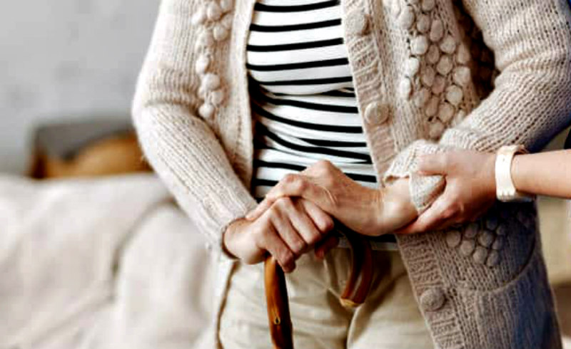 Young person gently holding elderly woman's hands