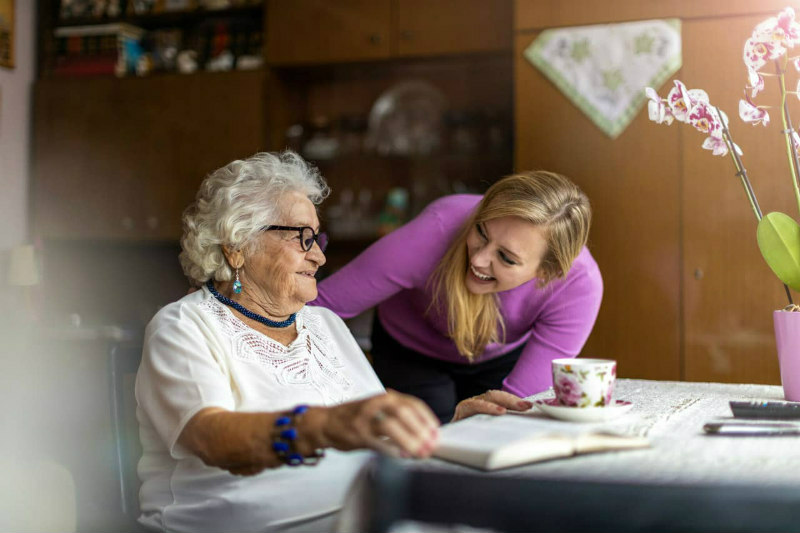 Young woman assisting elderly lady with reading at home