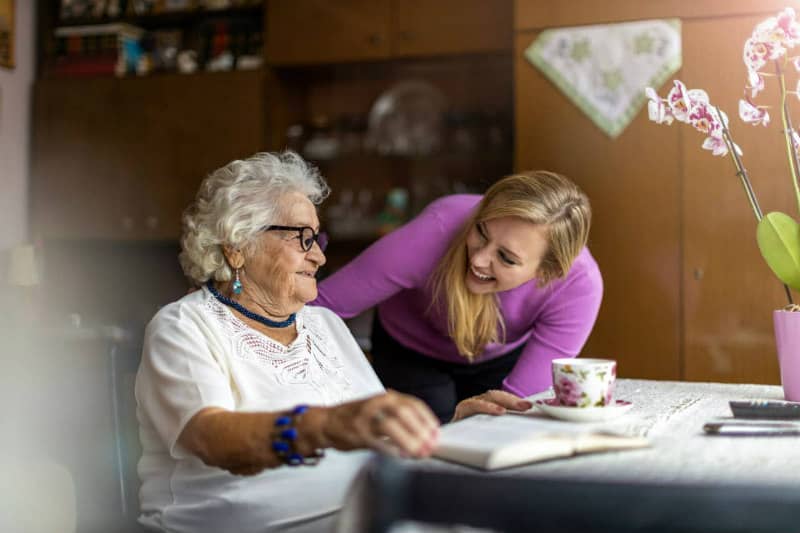 Live in carer assists elderly lady with reading at table