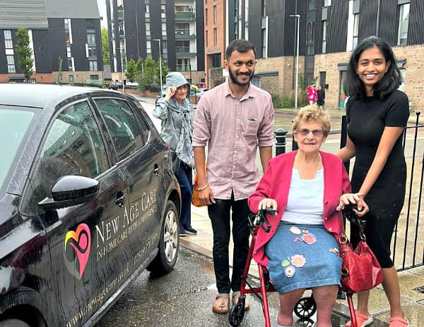 Elderly woman with walkers, assisted by carers