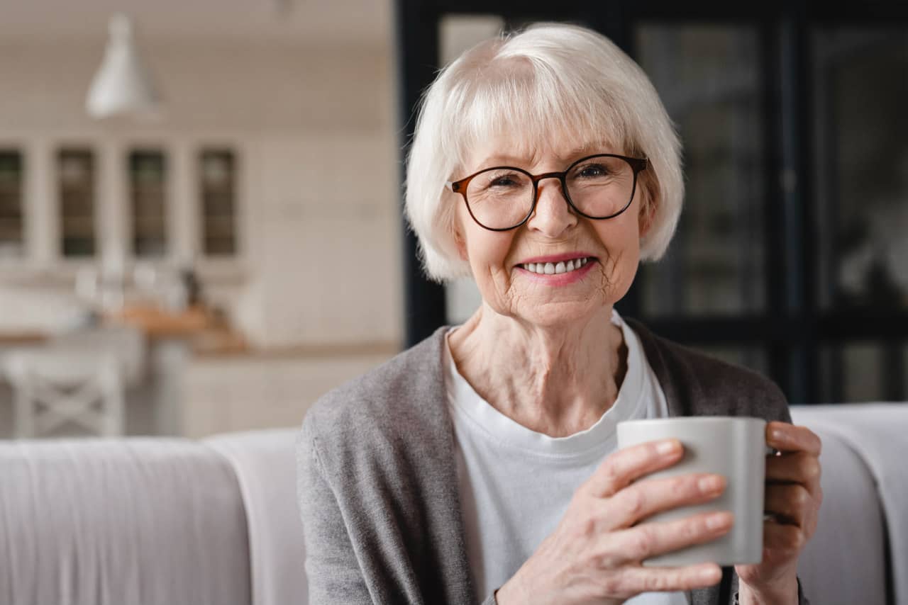 Smiling elderly woman holding a coffee mug indoors