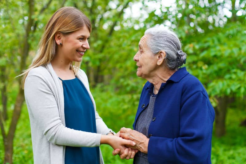 Young woman and elderly lady happily holding hands outdoors