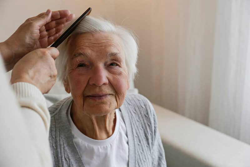 Elderly woman getting hair combed by caretaker