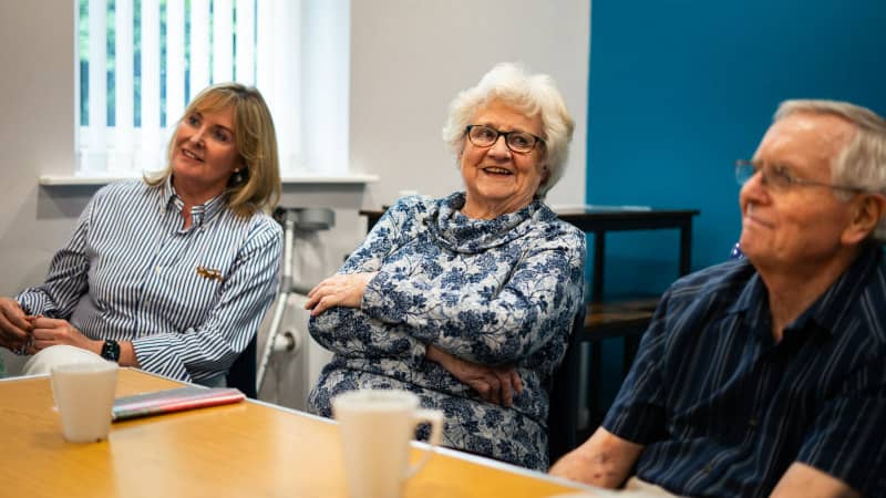 Three seniors laughing in a meeting with coffee