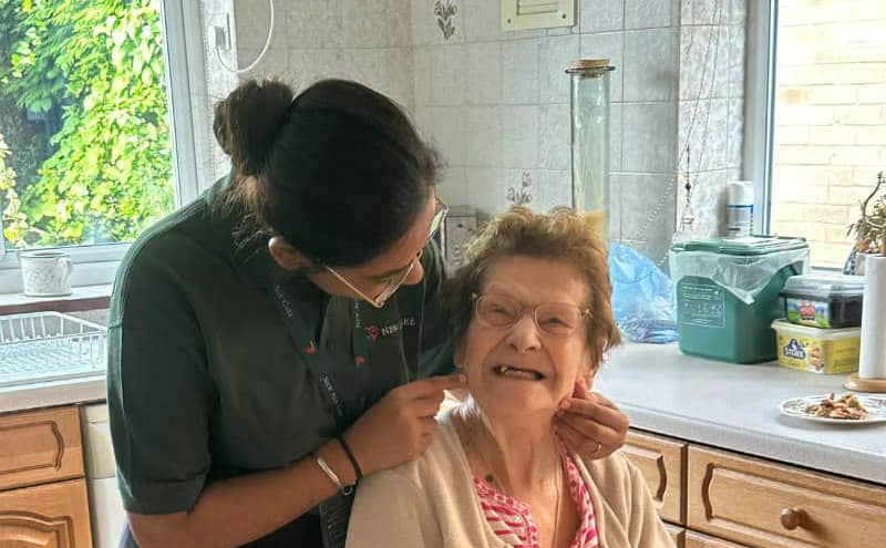 Caregiver assisting elderly woman in a sunny kitchen