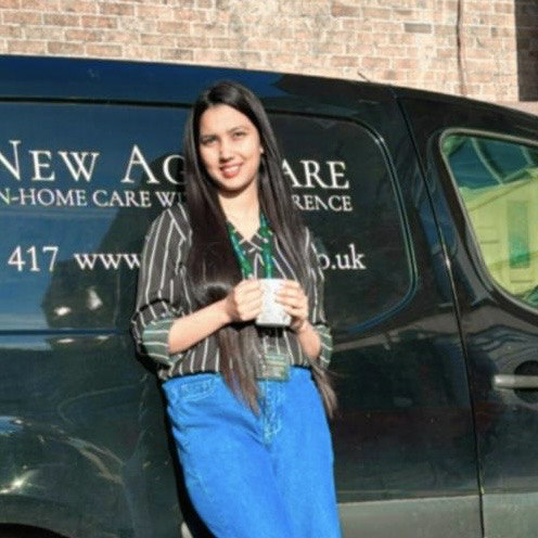 Woman standing beside 'New Agape Care' van, holding cup