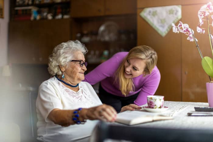 Young woman and elderly lady laughing with book and tea