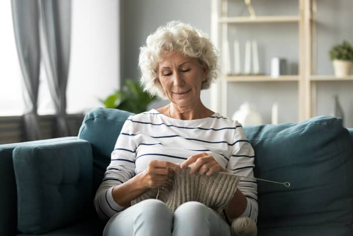 Elderly woman knitting on couch at home