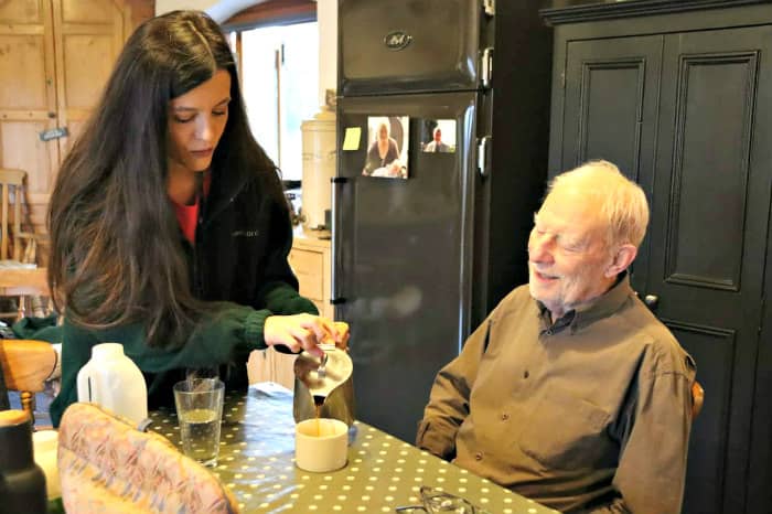 Woman serving coffee to elderly man at kitchen table